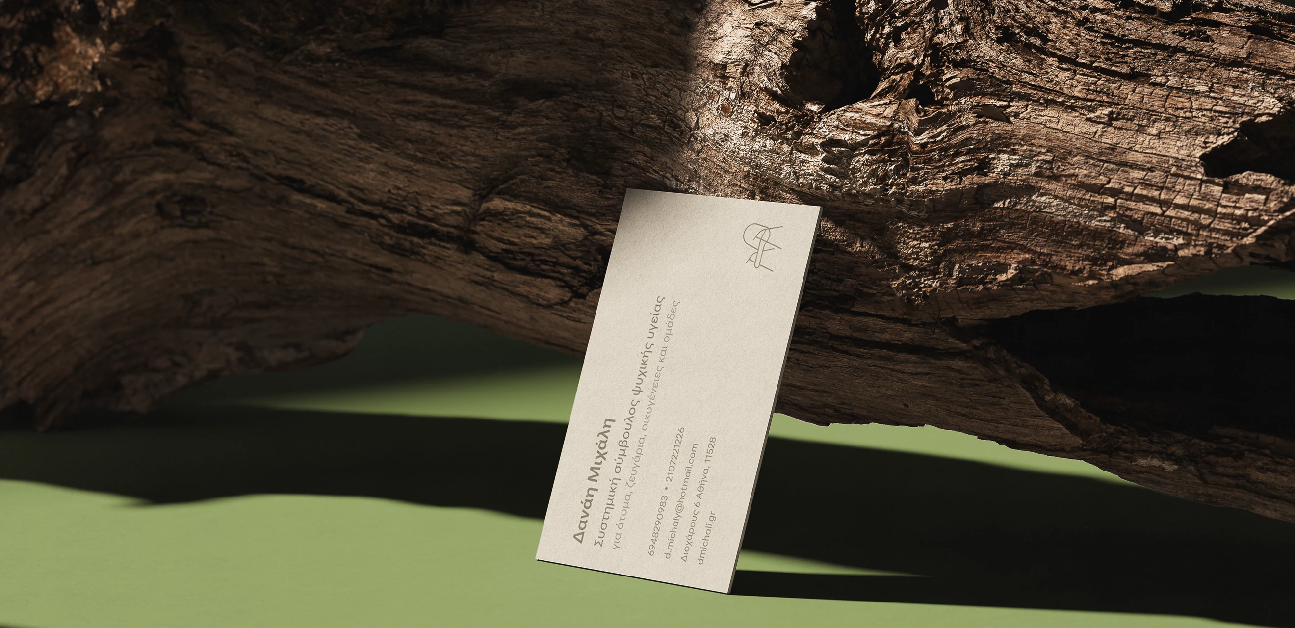 The back of the card propped against driftwood on a green ground, her name and what she practises set in Greek